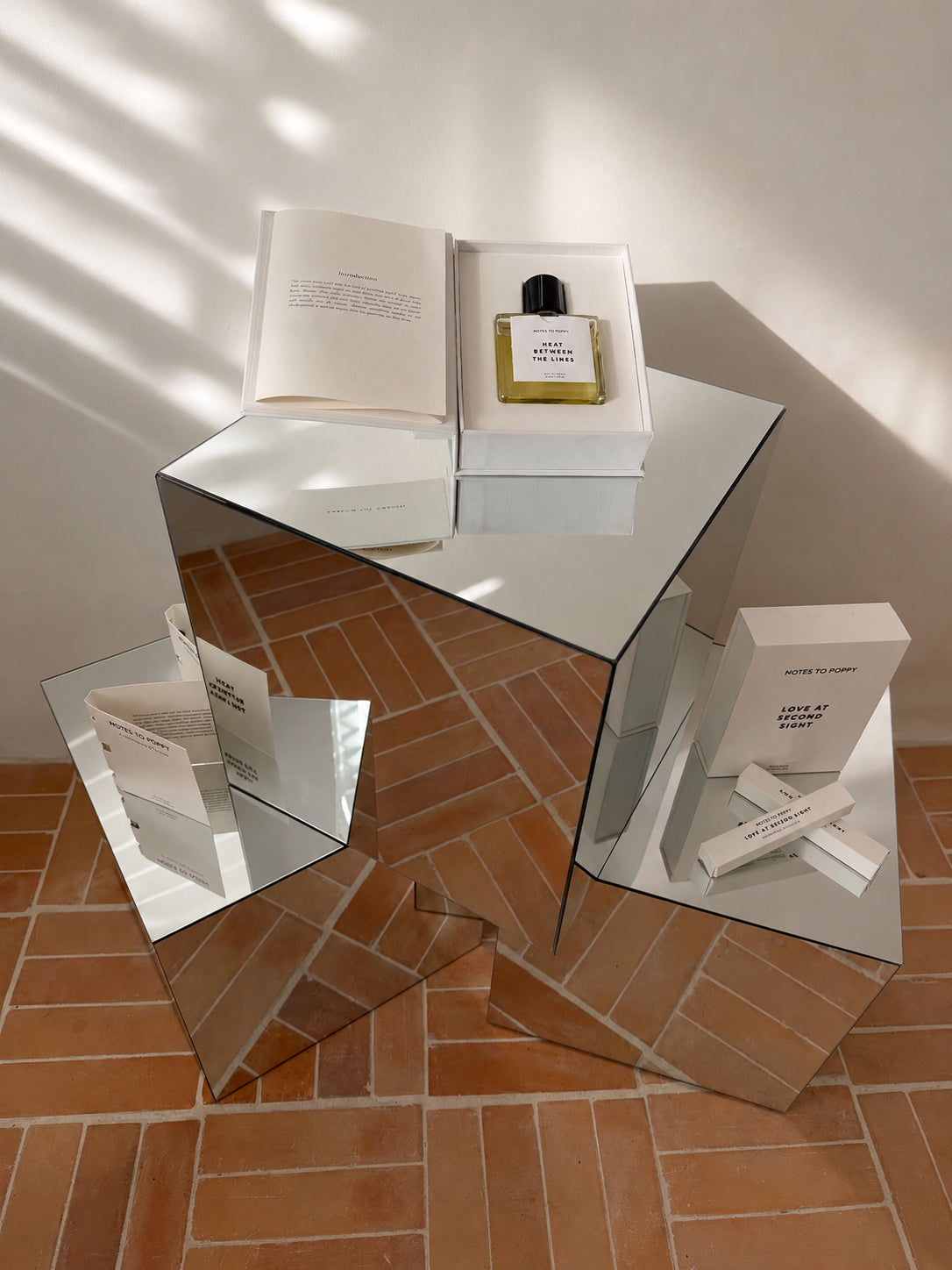 Notes To Poppy Australian perfume collection styled on a geometric mirror sculpture, terracotta tile floor, dramatic window light